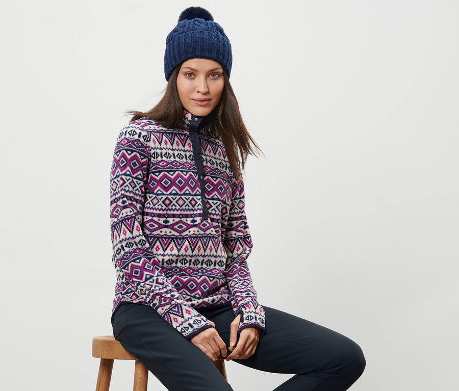 Nő ül egy széken, és egy mintás női mikropolár pulóvert és egy kék sapkát visel.