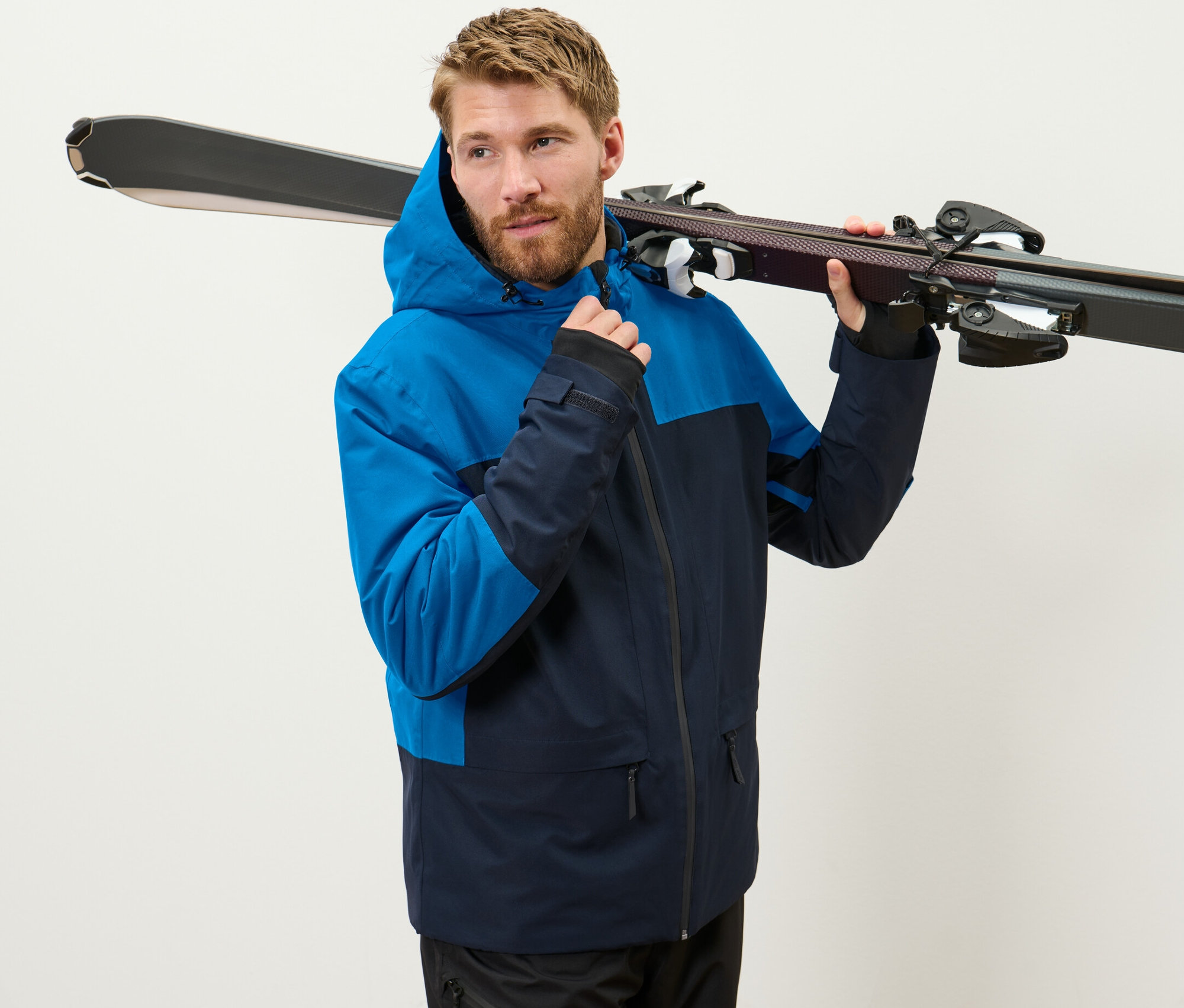 Férfi kék síkabátban síléceket tart a vállán.