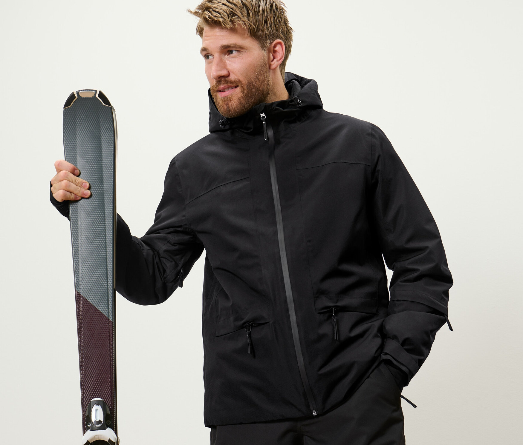 Férfi tart egy sílécet. Fekete síkabátot visel.