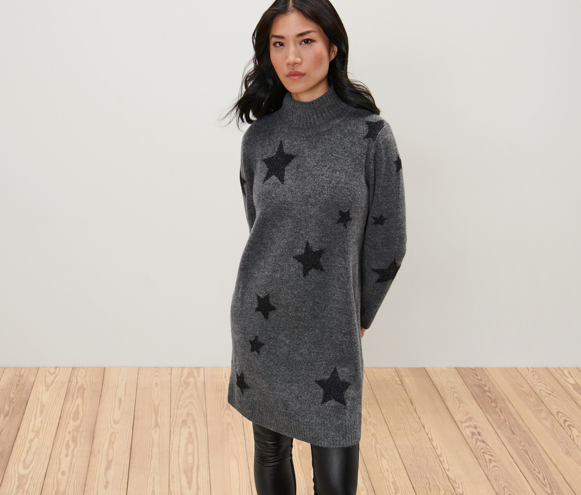 Nő pózol egy sötétszürke, csillagos kötött ruhában.