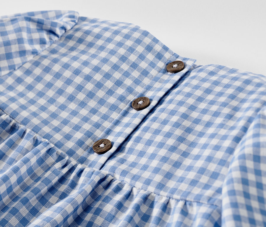 Egy kislány szövött ruha részlete kék-fehér kockás mintával és gombokkal.