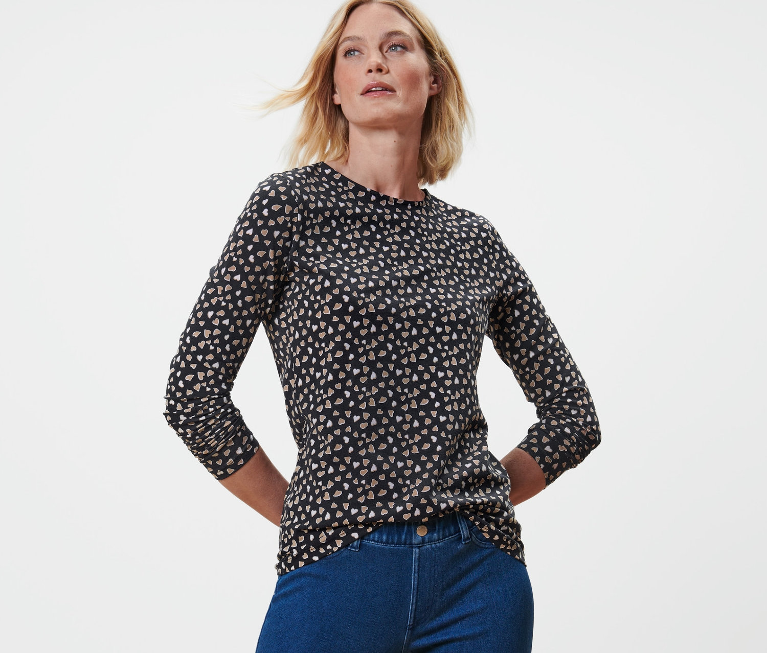 Egy szőke nő pózol egy mintás hosszú ujjú felsőben és kék farmerban.