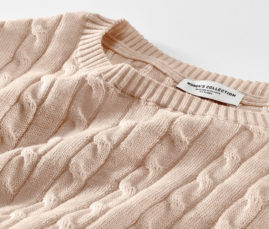 Egy krémszínű, fonott mintás kötött pulóver részlete.