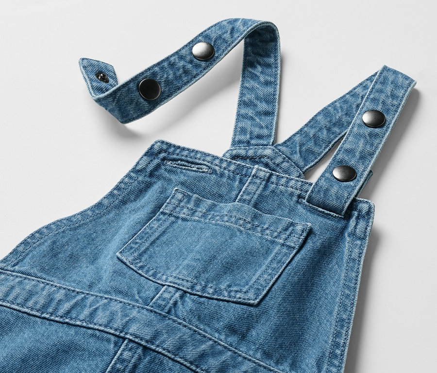 Gyerek kötényruha mellzsebbel és gombos, állítható pántokkal.