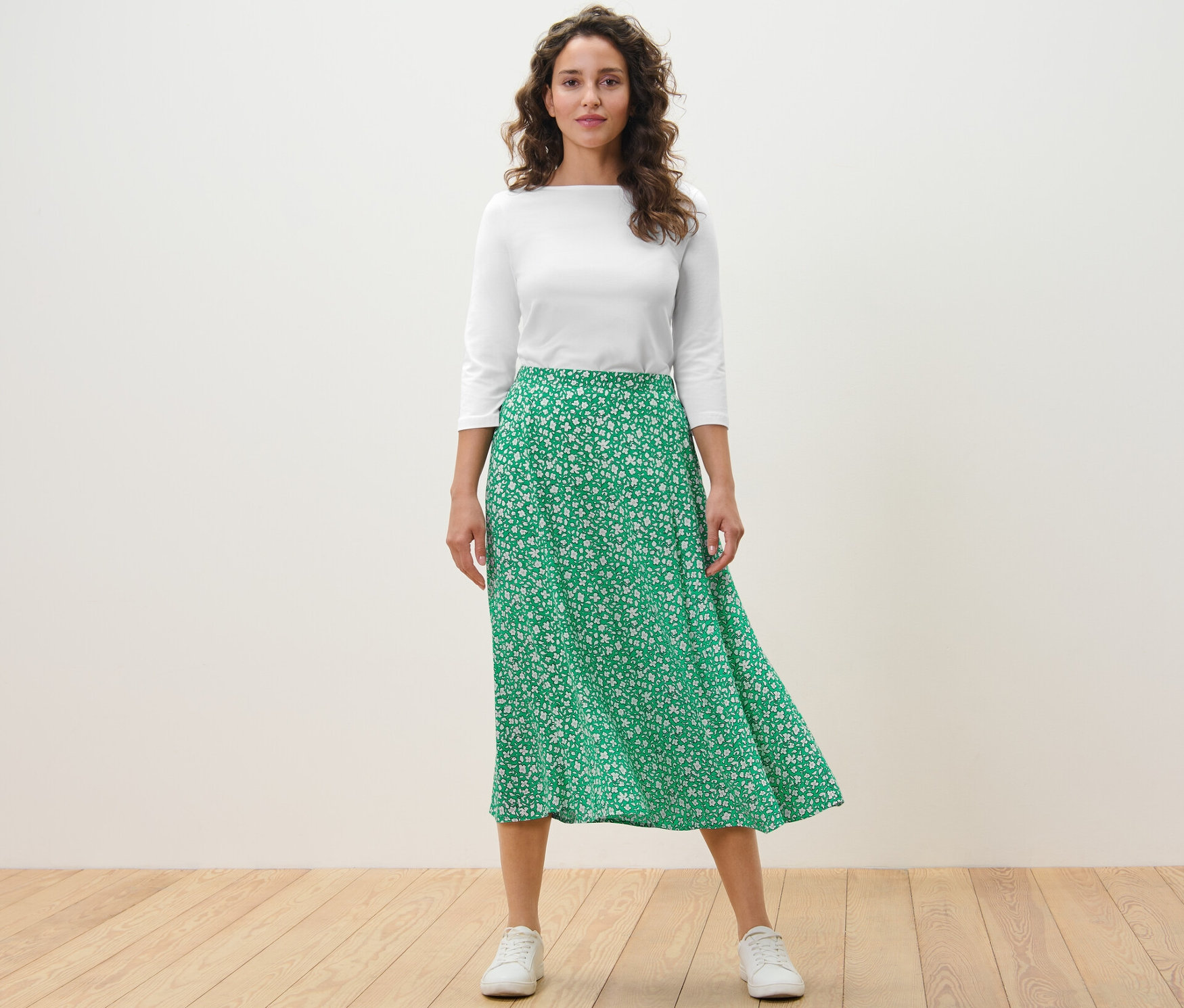 Nő áll, és virágos, zöld, női szövött midiszoknyát visel.