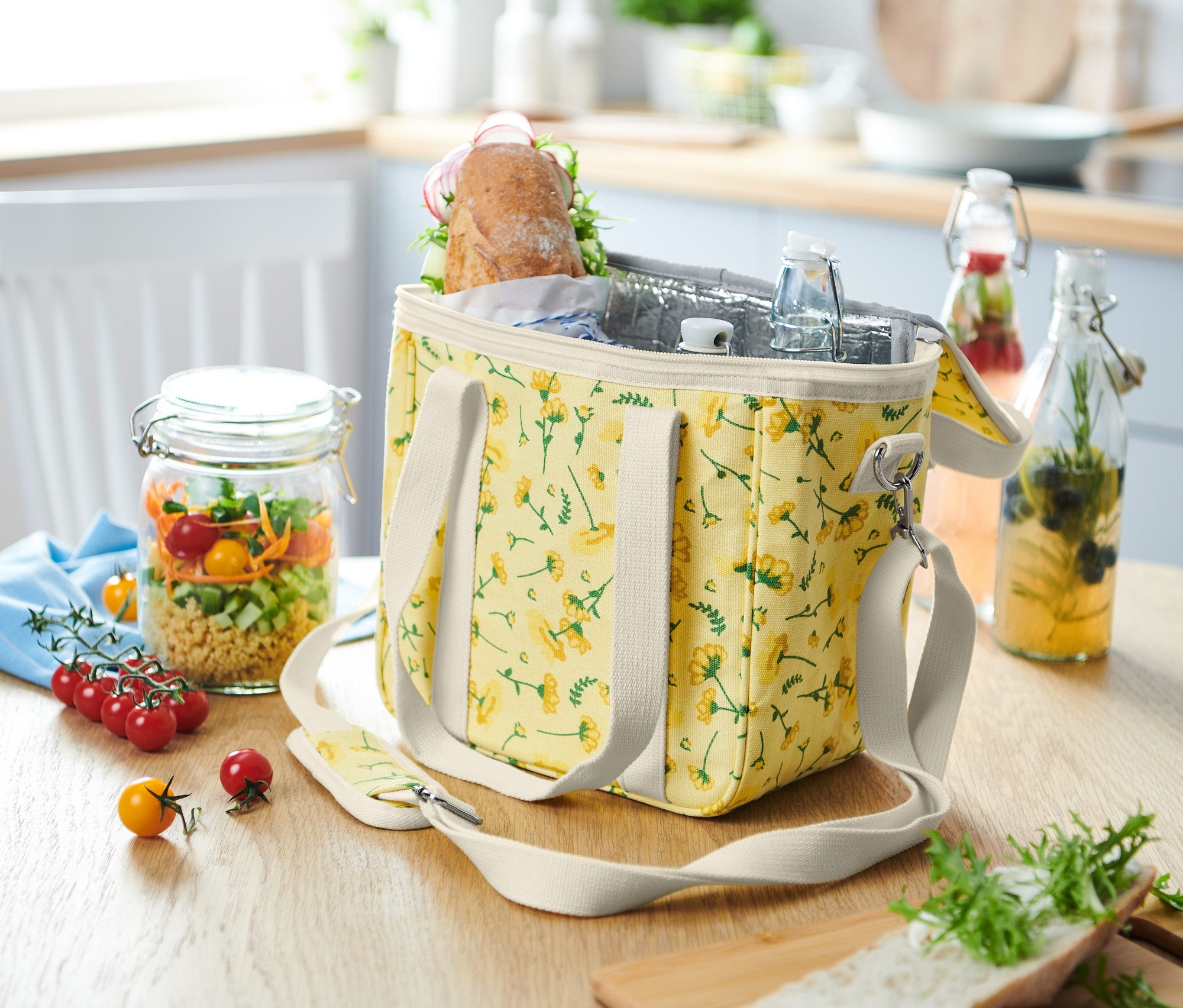 Virágos ételhordó hűtőtáska áll egy asztalon egy salátás üveg mellett.
