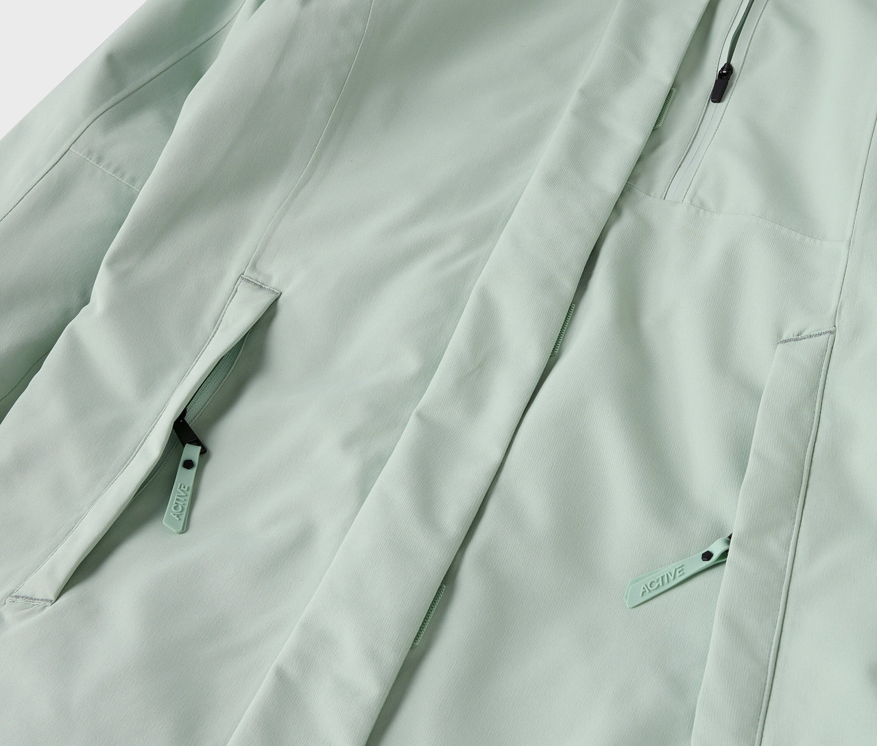 Világoszöld kabát részlete cipzáras zsebekkel.