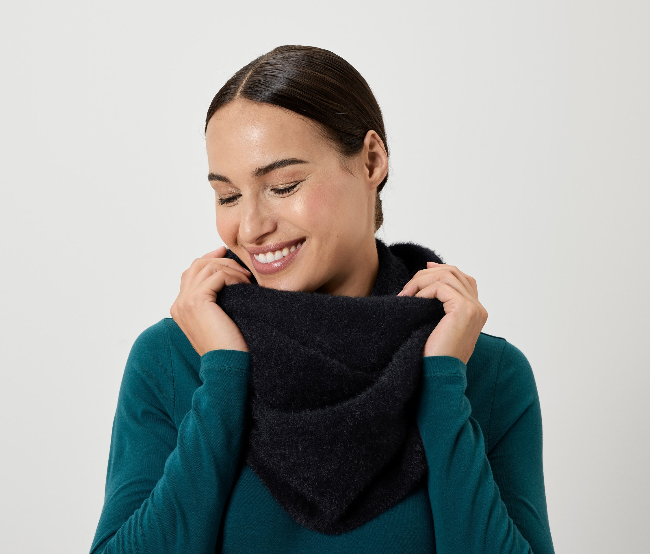 Mosolygó nő lefelé néz, és kezével fekete kendőt tart a nyaka körül.