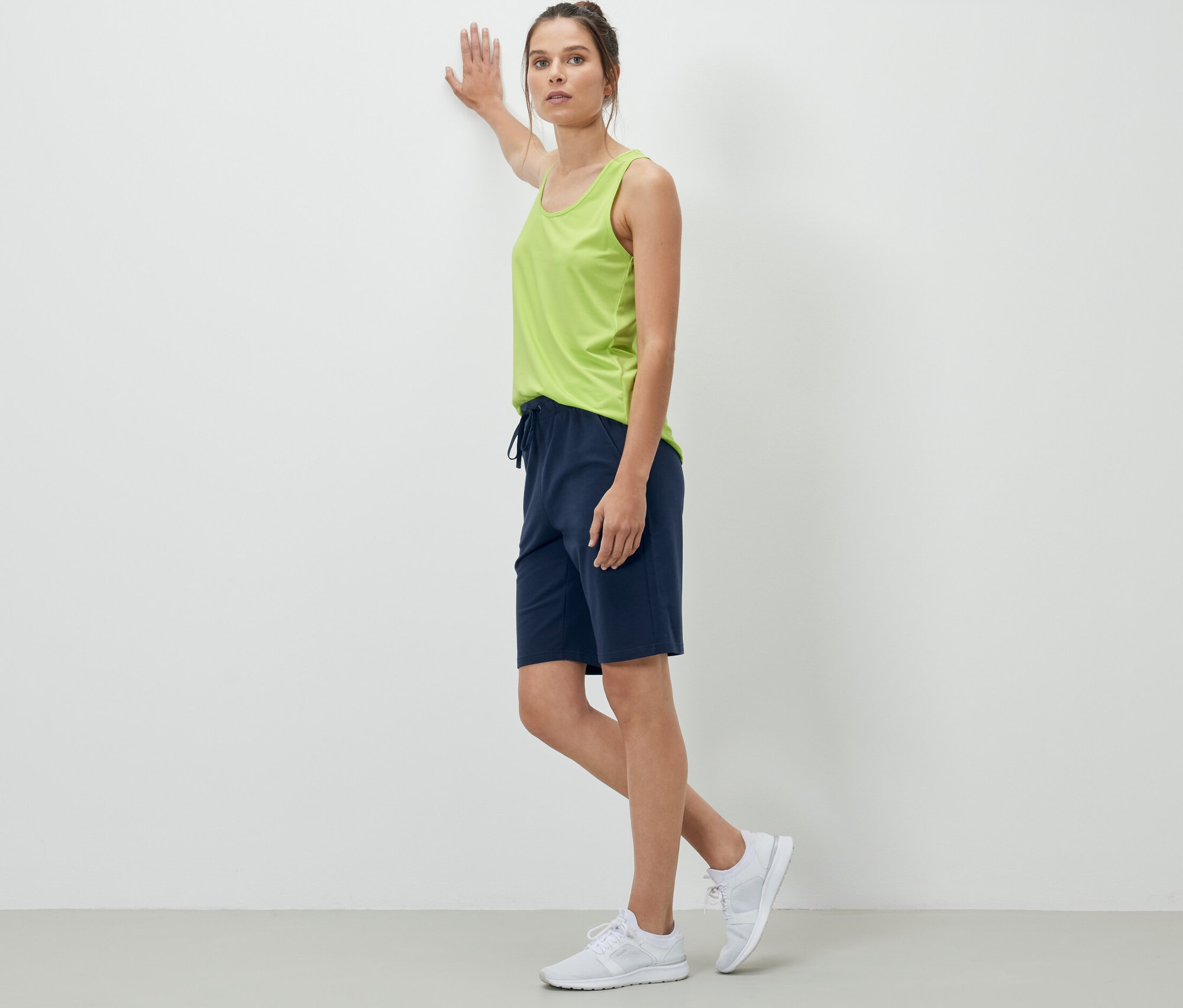 A falnak dőlő nő sötétkék rövid szabadidőnadrágot visel.