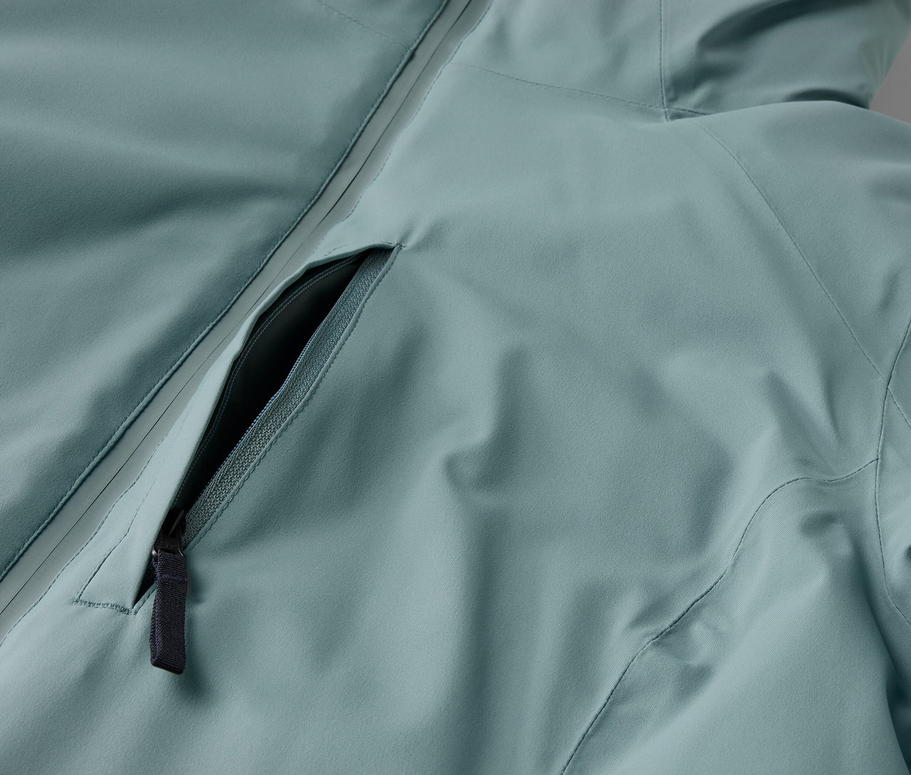 Világoskék kabát részlete fekete cipzárral.