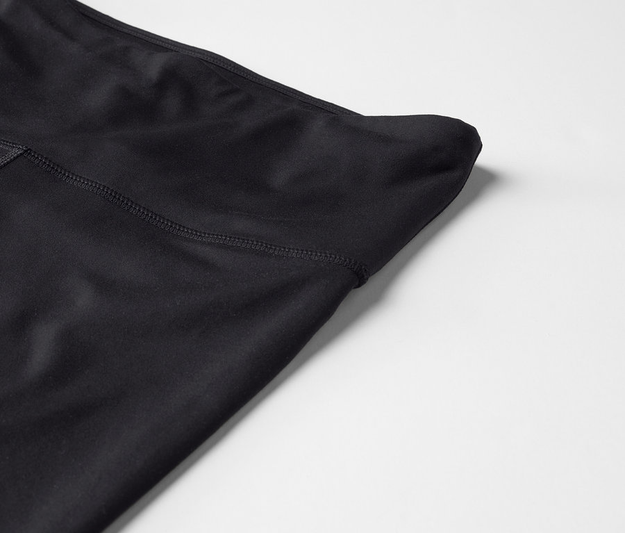 Egy fekete, magas derekú leggings részletfotója fehér háttéren.