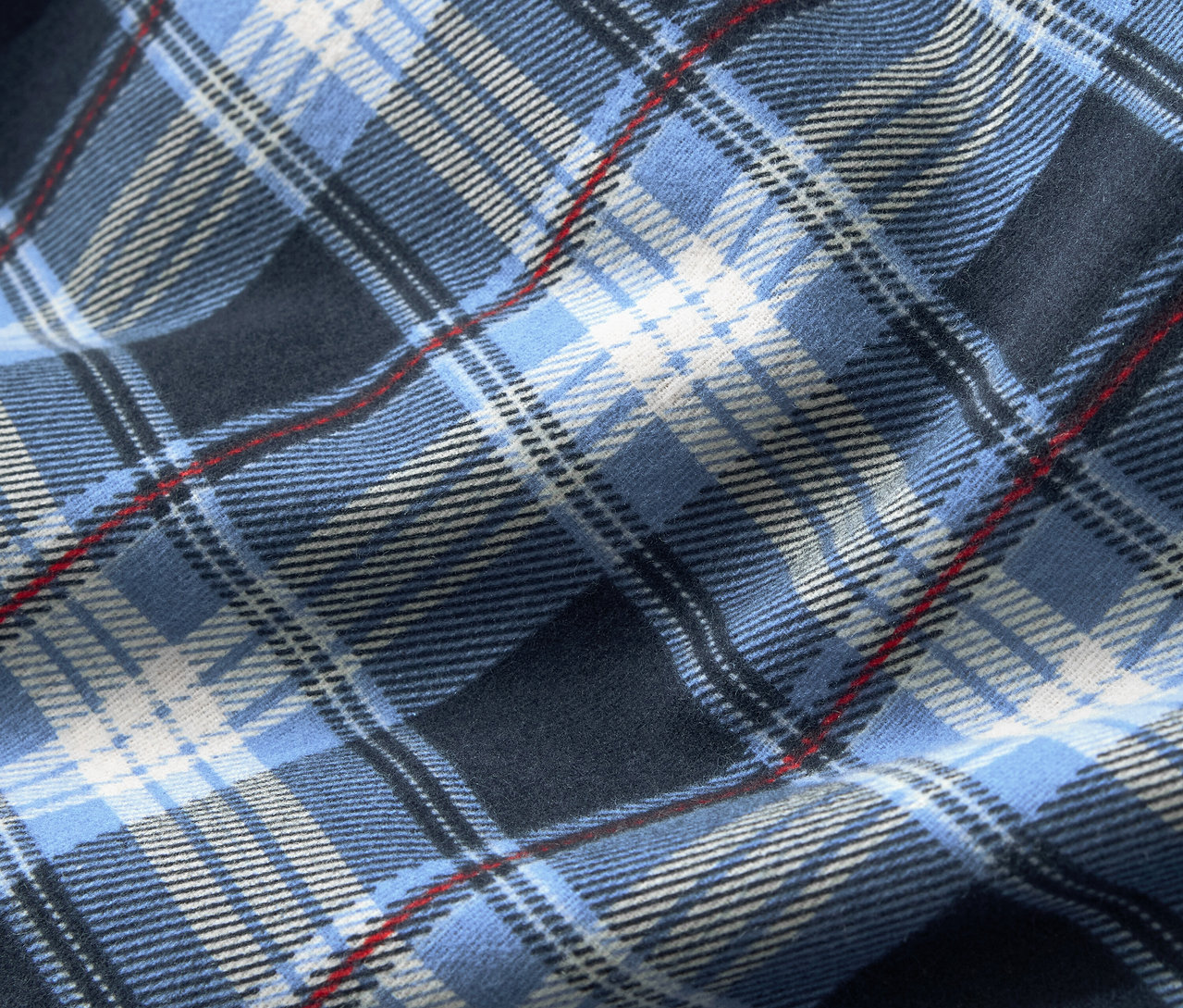 Közeli kép egy kék kockás mintázatú szövetről, amelyet fehér és vékony piros csíkok egészítenek ki.