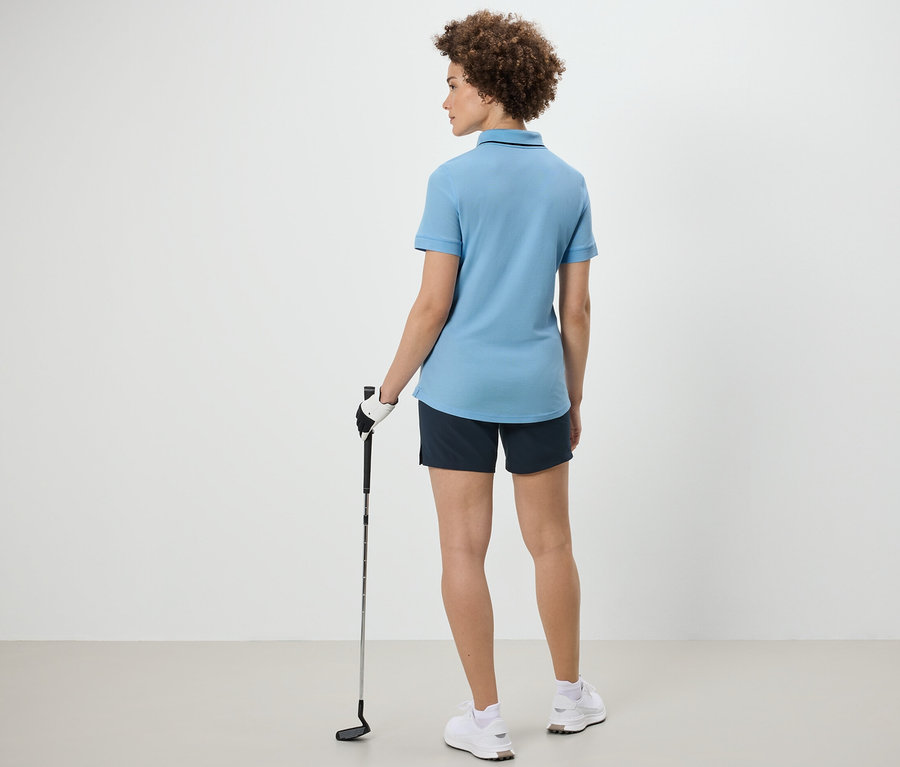 Hátulról látható nő golfütőt tart, világoskék funkcionális pólóinget visel.