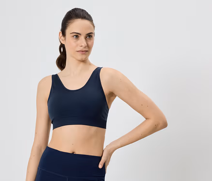 Lófarkas nő, tengerészkék sportmelltartót és leggingset visel, kezét a csípőjére teszi.