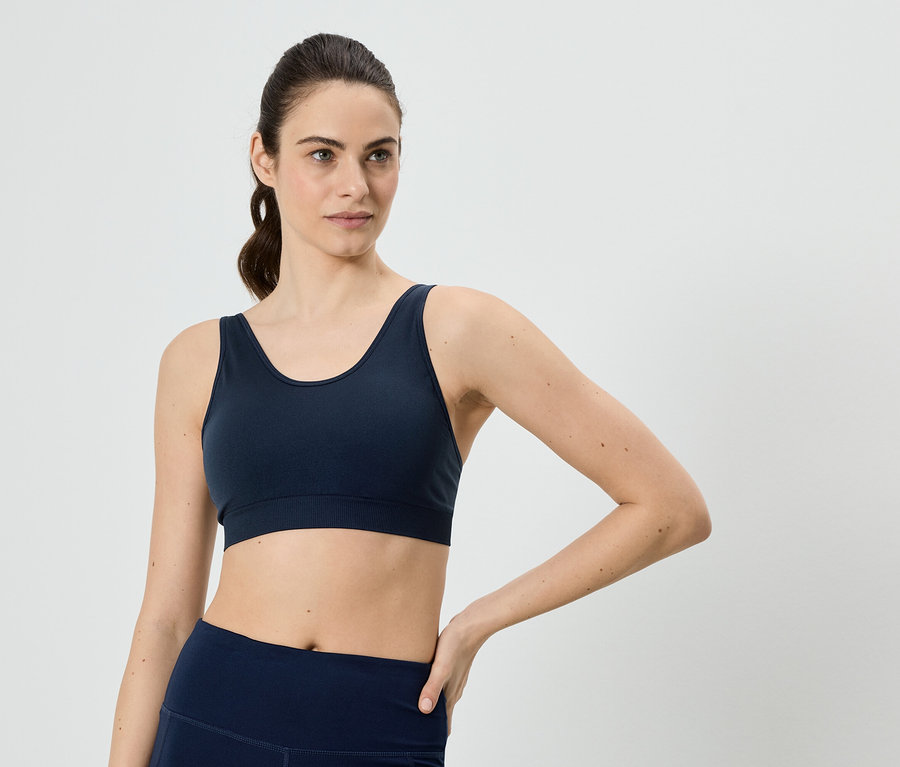 Lófarkas nő, tengerészkék sportmelltartót és leggingset visel, kezét a csípőjére teszi.