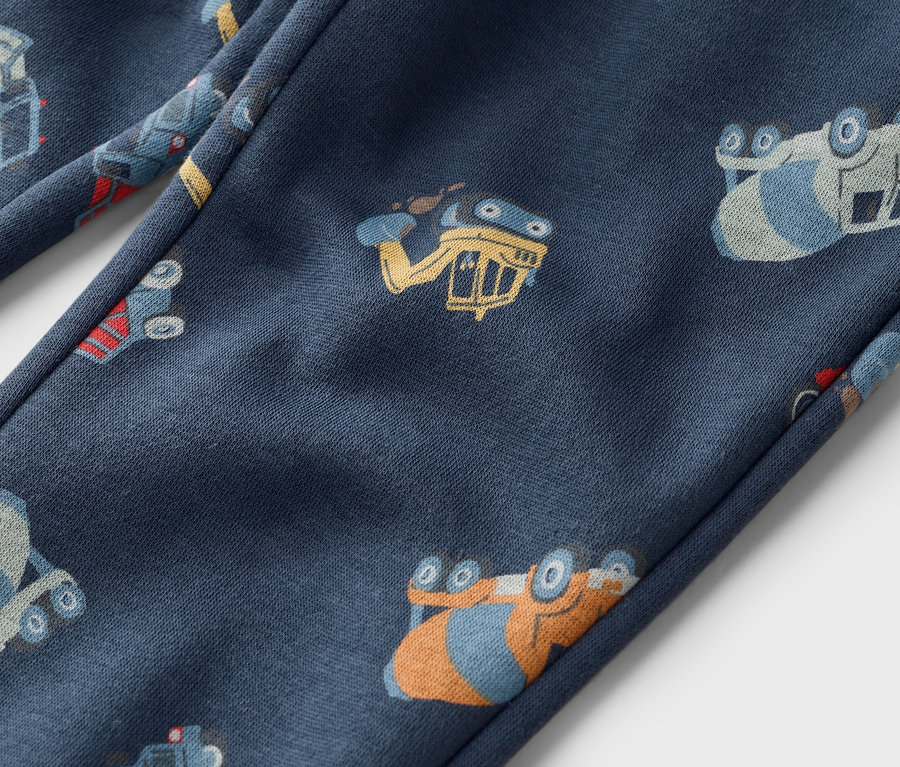 Egy sötétkék nadrág közeli képe, melyet munkagépek mintája borít.