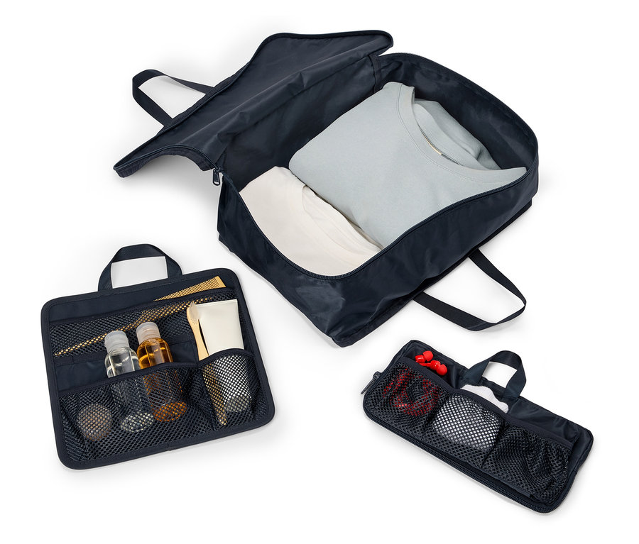 Három nyitott, tengerészkék utazótáska fogantyúkkal és cipzárral elrendezve egy fehér háttéren. A táskák ruhákat, kozmetikumokat és kiegészítőket tartalmaznak.