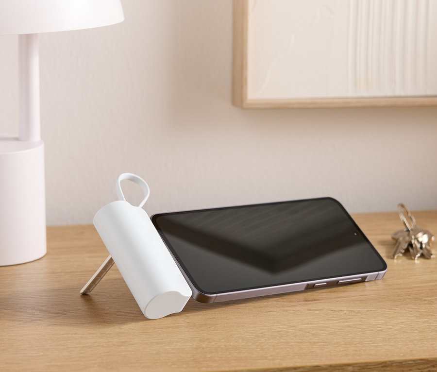 Egy fa asztalon áll egy lámpa, egy tablet, egy kulcstartó és egy fehér, hengeres tárgy fogantyúval.