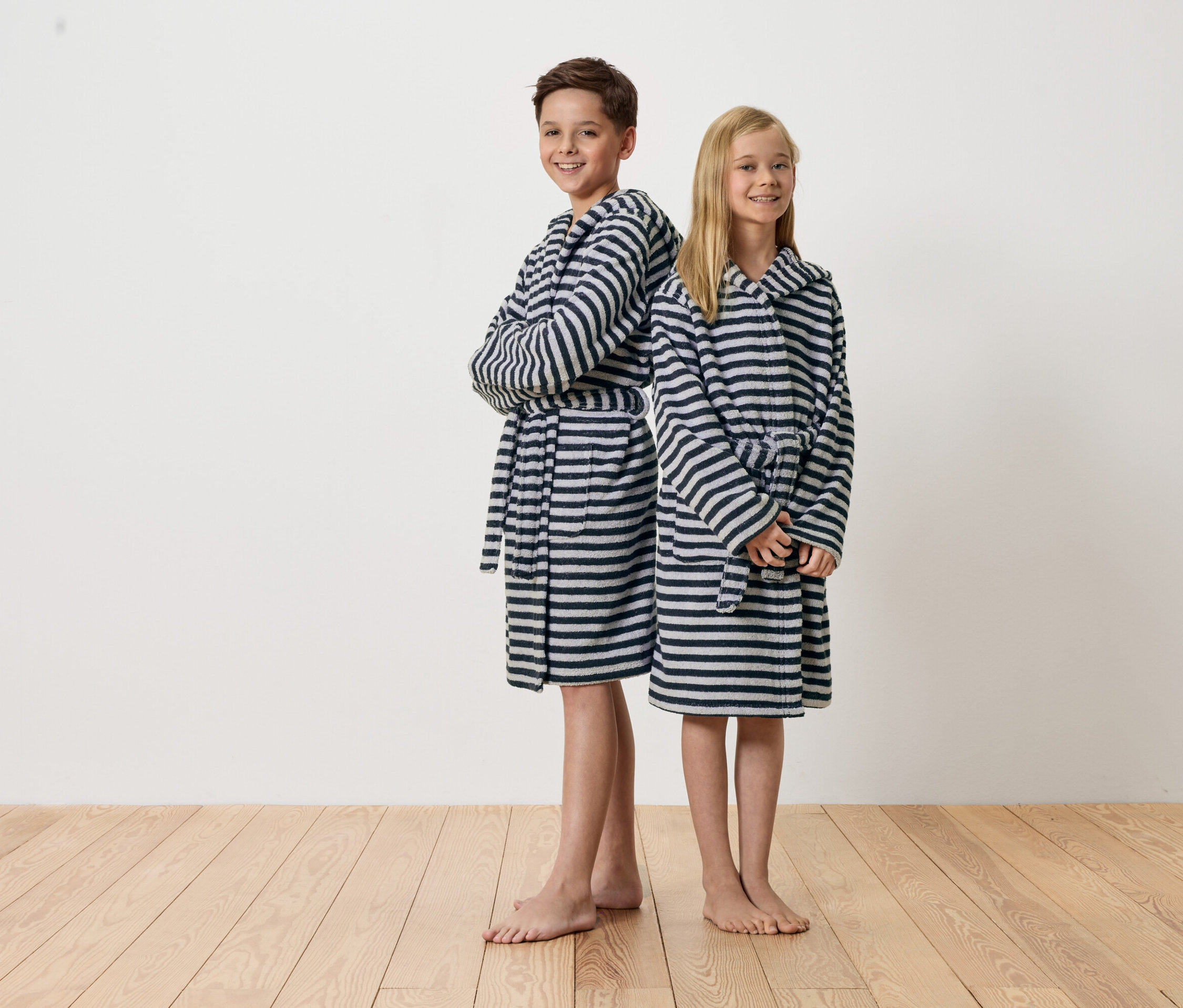 Egy fiú és egy lány háttal állnak egymásnak, csíkos fürdőköpenyben.