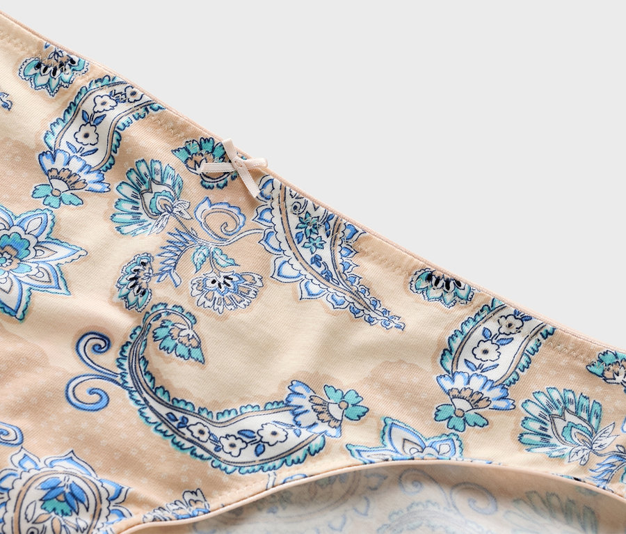 Közeli kép egy bézs színű, kék paisley mintás és masnis bugyiról.