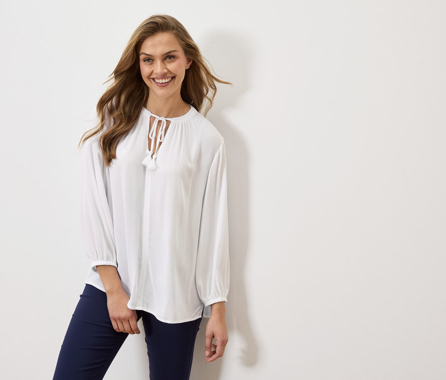 Nő visel egy hosszú ujjú, fehér blúzt és egy sötétkék nadrágot.