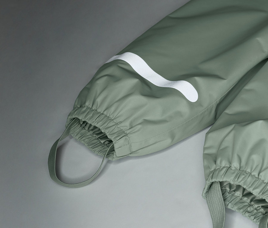 Közeli kép egy világoszöld esőnadrágról, fehér logóval és rugalmas mandzsettákkal.