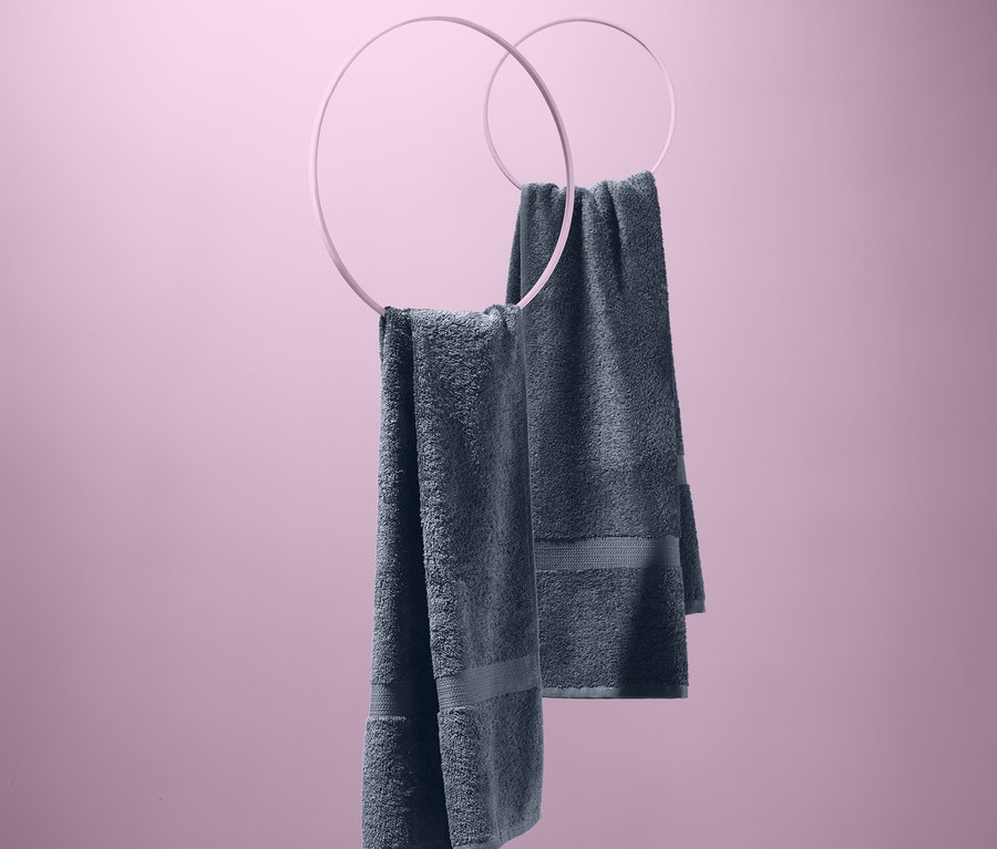 Két szürke törölköző szettben lóg rózsaszín háttér előtt, kör alakú tartókon.
