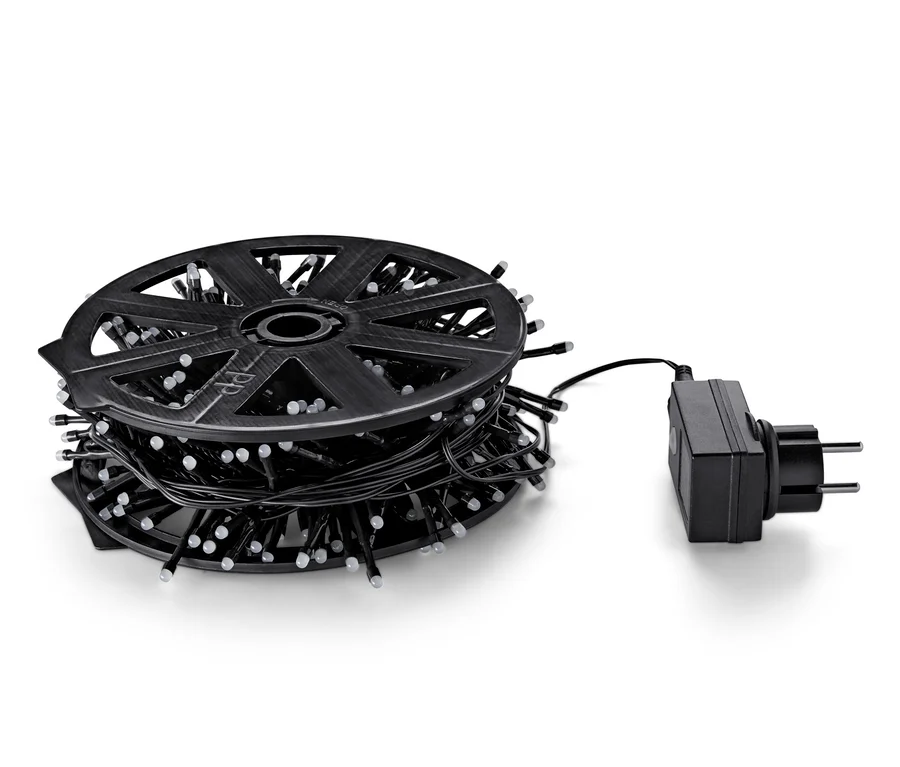 Egy fekete LED-es kültéri égősor feltekerve egy tekercsre, mellette egy hálózati adapter.