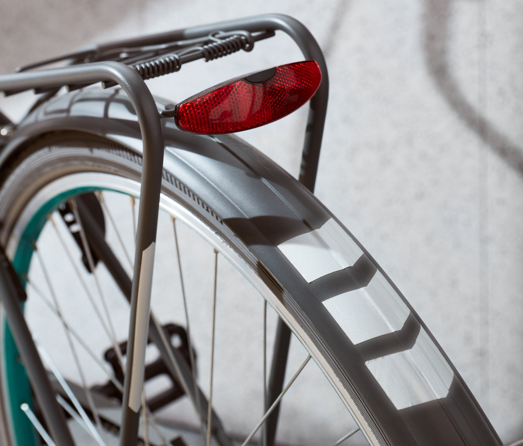 Egy kerékpár hátsó kerekének részlete piros lámpával és fényvisszaverő matricakészlettel.