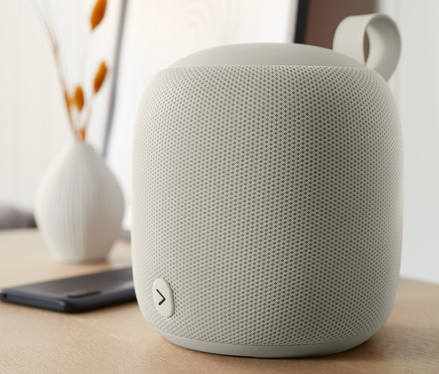 Egy szürke, közepes méretű Fabric Bluetooth® hangszóró az asztalon.