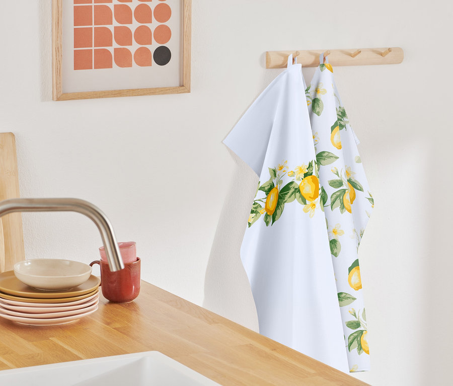 Két citrom mintás konyharuha lóg egy fa akasztón.