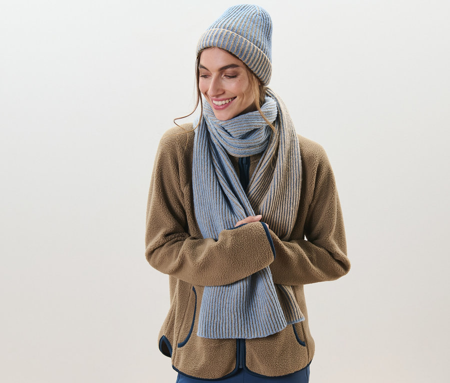Nő mosolyog, kötött sálat és sapkát visel.