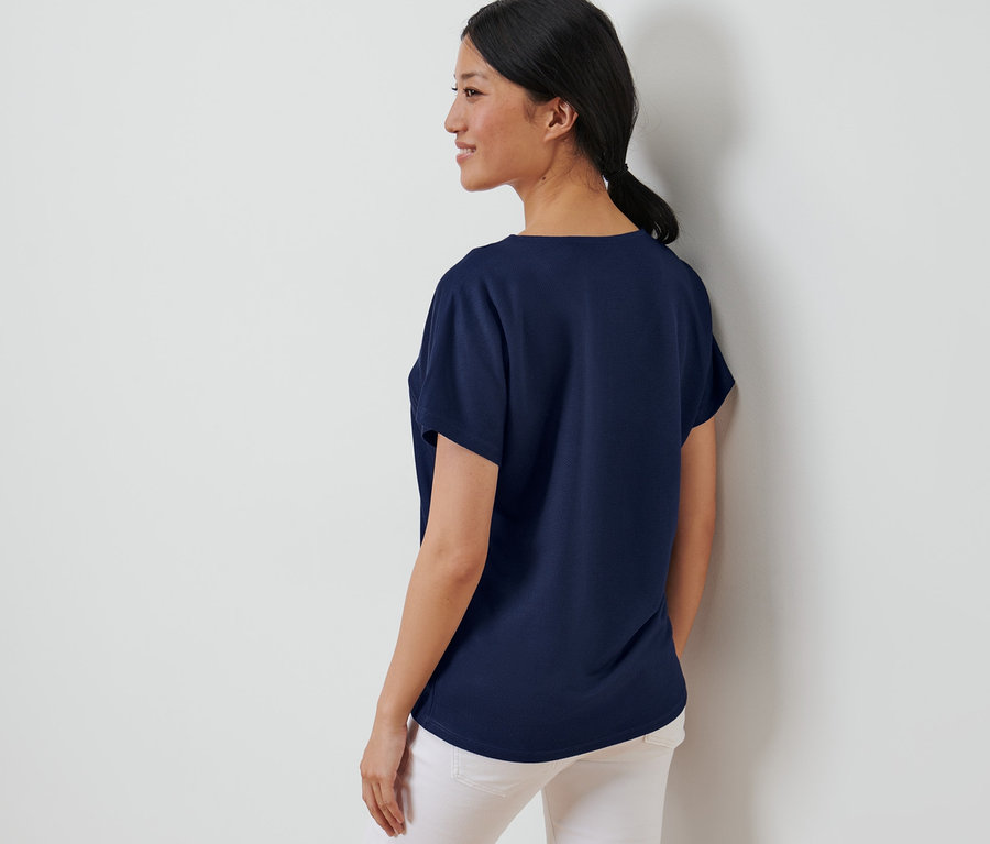 Nő pózol egy sötétkék, strukturált felsőben.