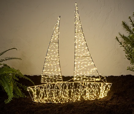 Egy megvilágított 3D-s LED-es kültéri csónak áll a földön növények mellett.