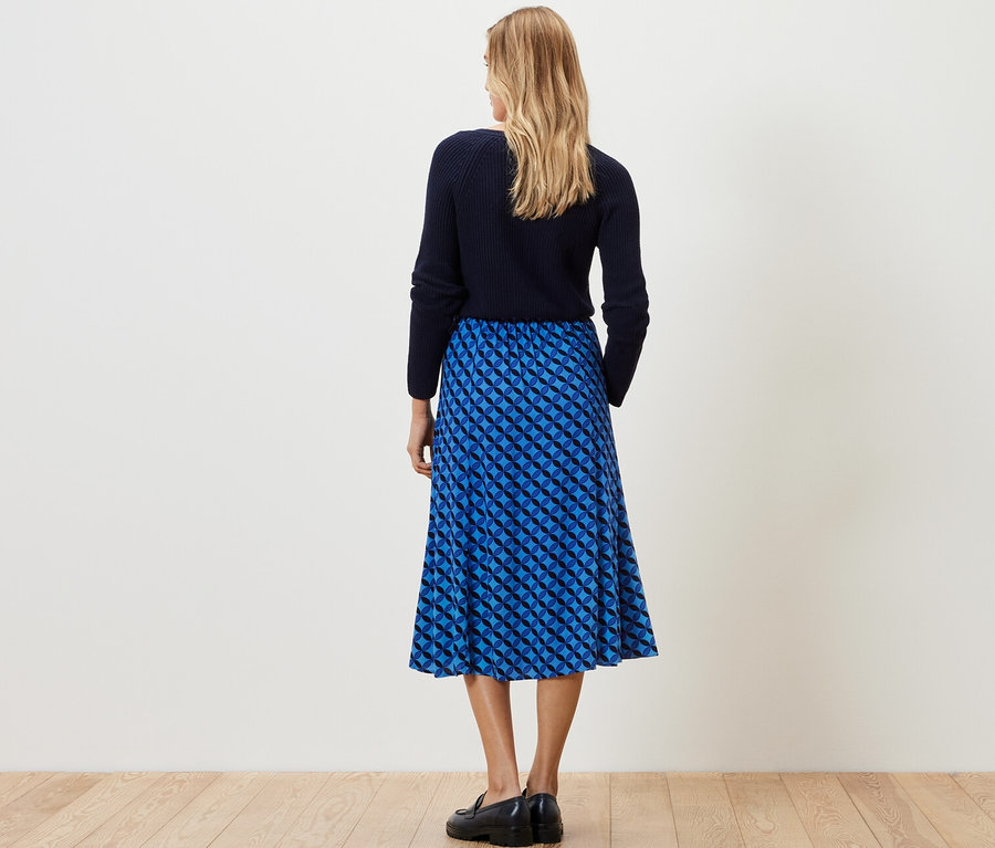 Egy nő háttal áll a kamerának, és egy sötétkék, mintás midi szoknyát visel.