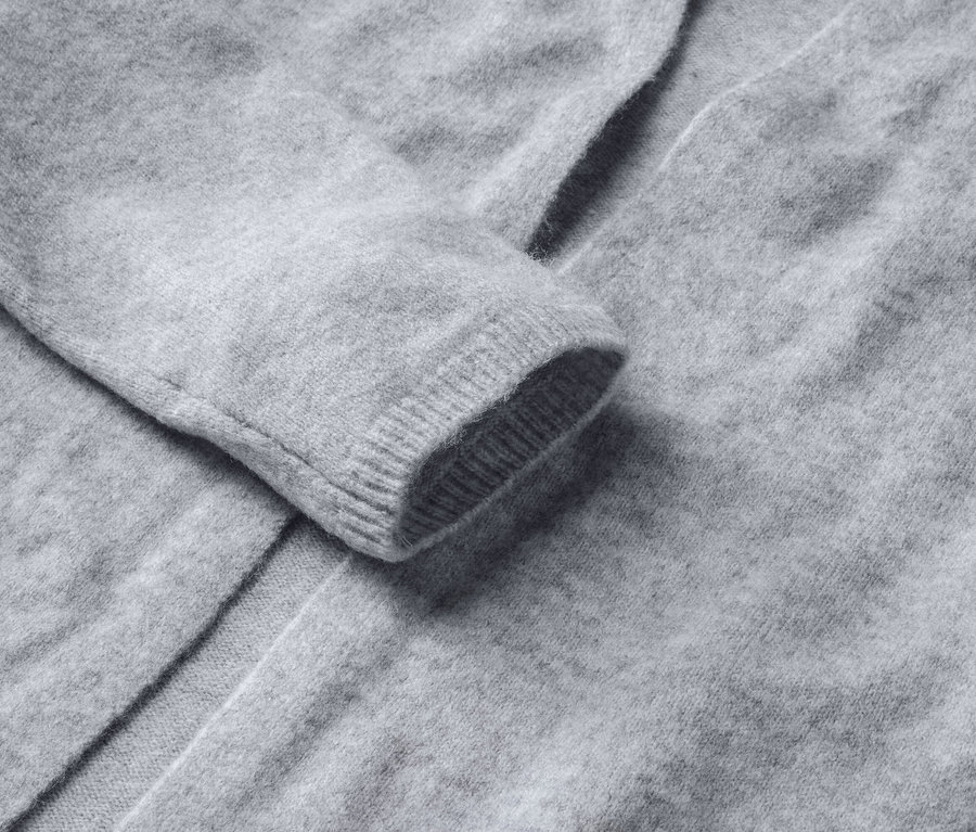 Egy szürke, nyitott kötött kardigán részlete.