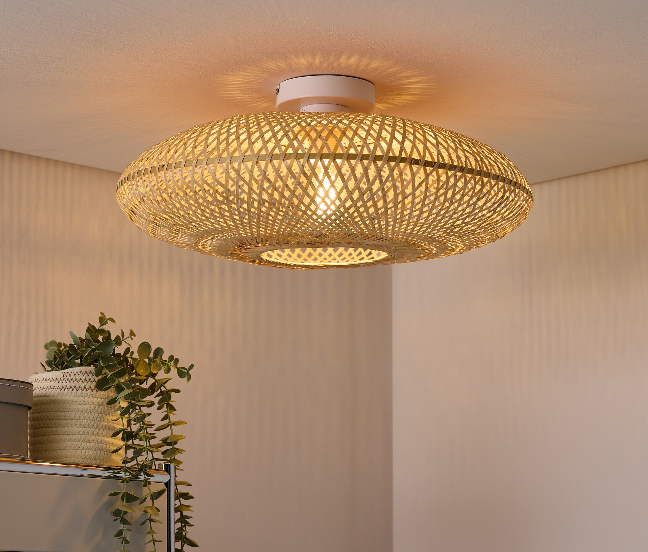 Fonott mennyezeti lámpa fehér mennyezeten, alatta egy cserepes növény és egy szürke bőrönd.