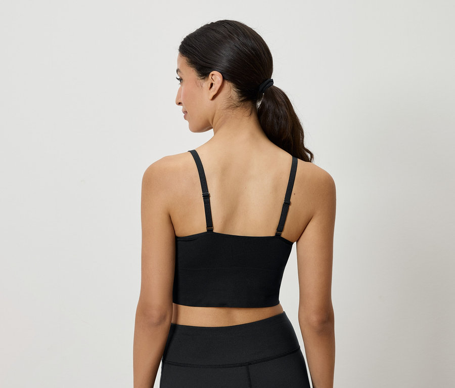 Hátulnézet egy barna hajú, lófarokba kötött nőről, aki fekete sportmelltartót és leggingset visel.