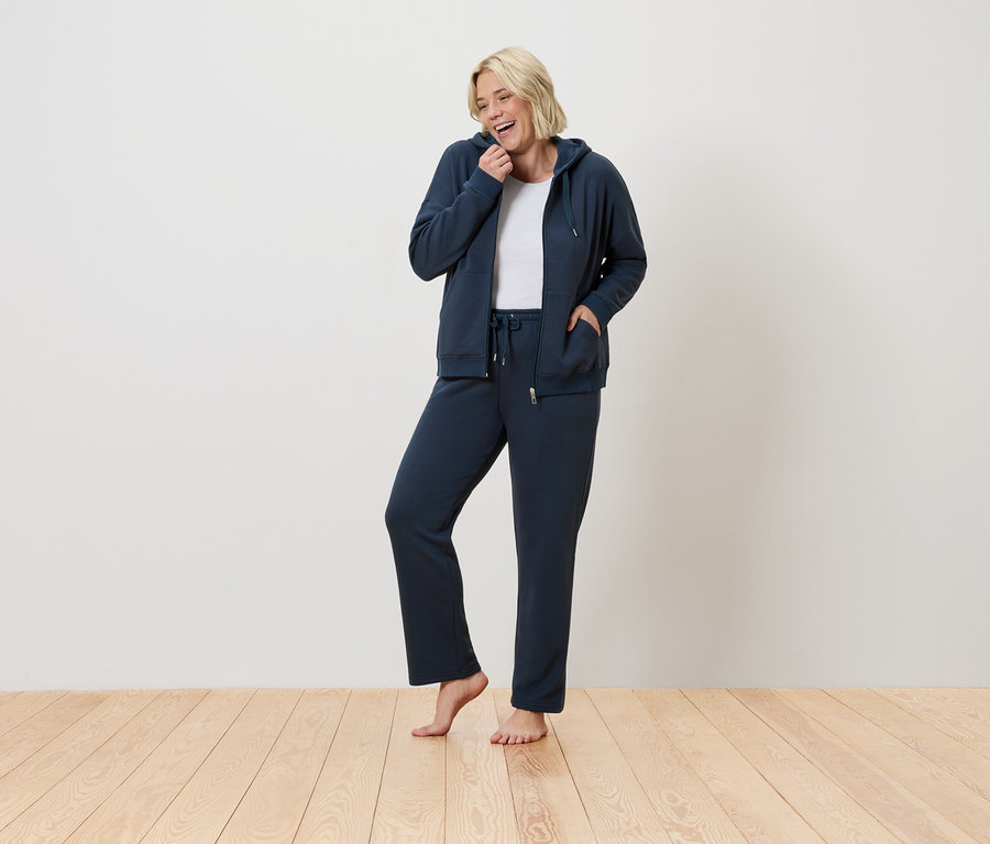 Egy nő áll és mosolyog, kék tréningruhát visel.