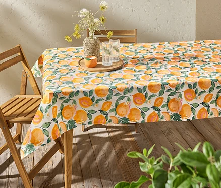 Citrusmintás, letörölhető asztalterítővel terített asztal, rajta váza virágokkal és vizespoharak.