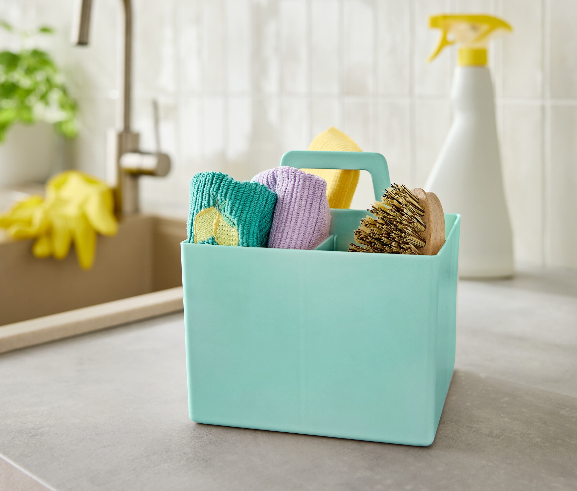 Egy türkizkék doboz tisztítószerekkel egy szürke pulton áll a mosogató mellett.