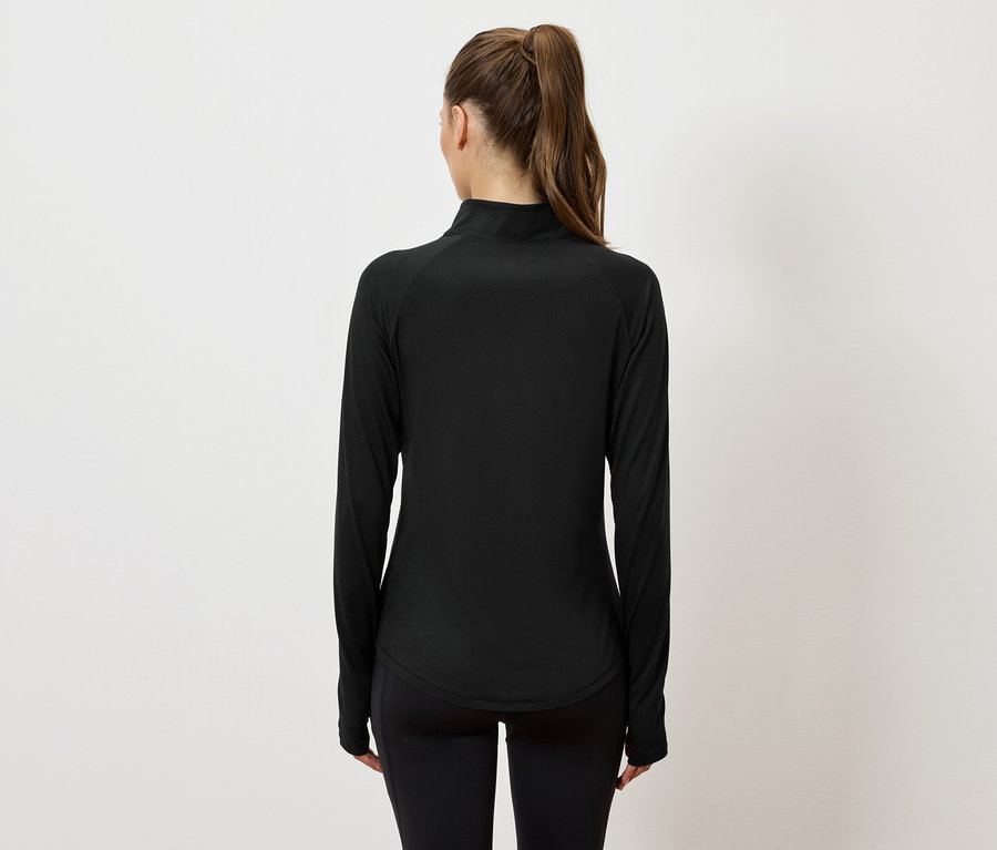 Hátulnézet egy copfos nőről, aki fekete, hosszú ujjú sportfelsőt és fekete leggingset visel.
