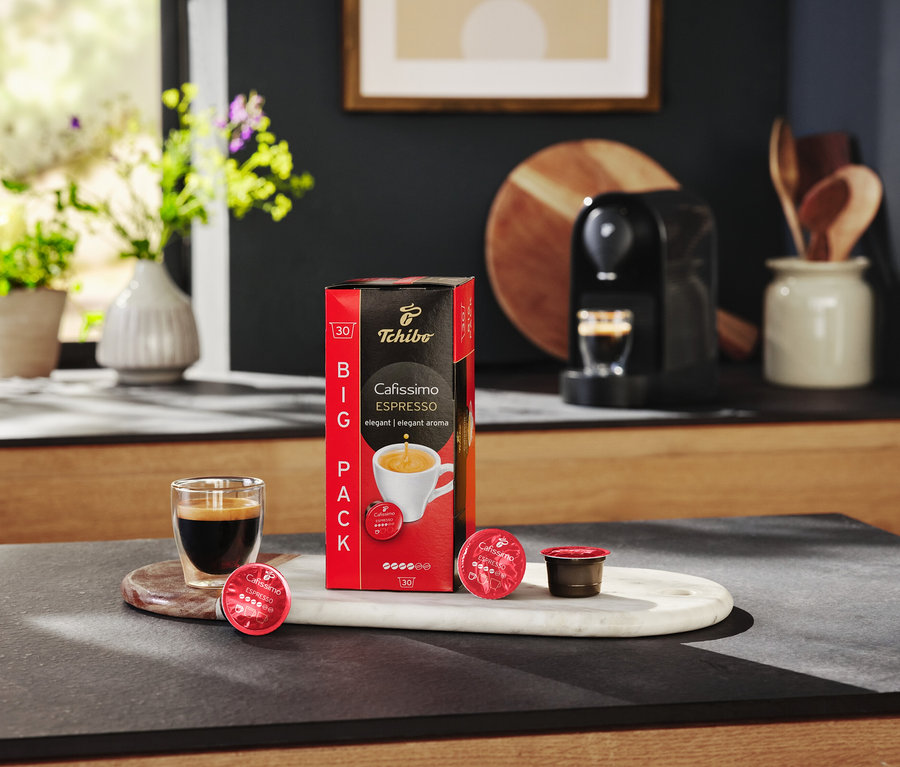 Az asztalon egy csomag Cafissimo Espresso kapszula, egy eszpresszóval teli pohár és egy kávéfőző található.