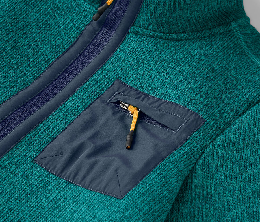 Egy türkizkék színű fleece pulóver részlete, cipzáras mellzsebbel.