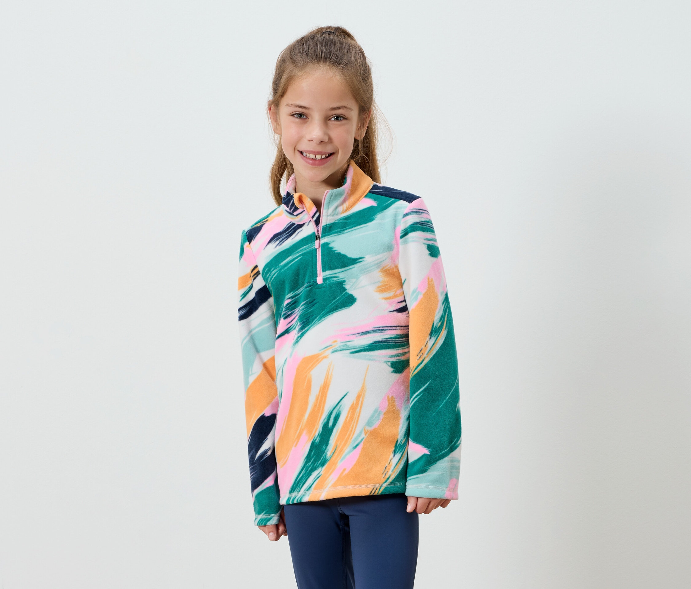 Egy mosolygó lány absztrakt mintás polárfelsőt és kék nadrágot visel.