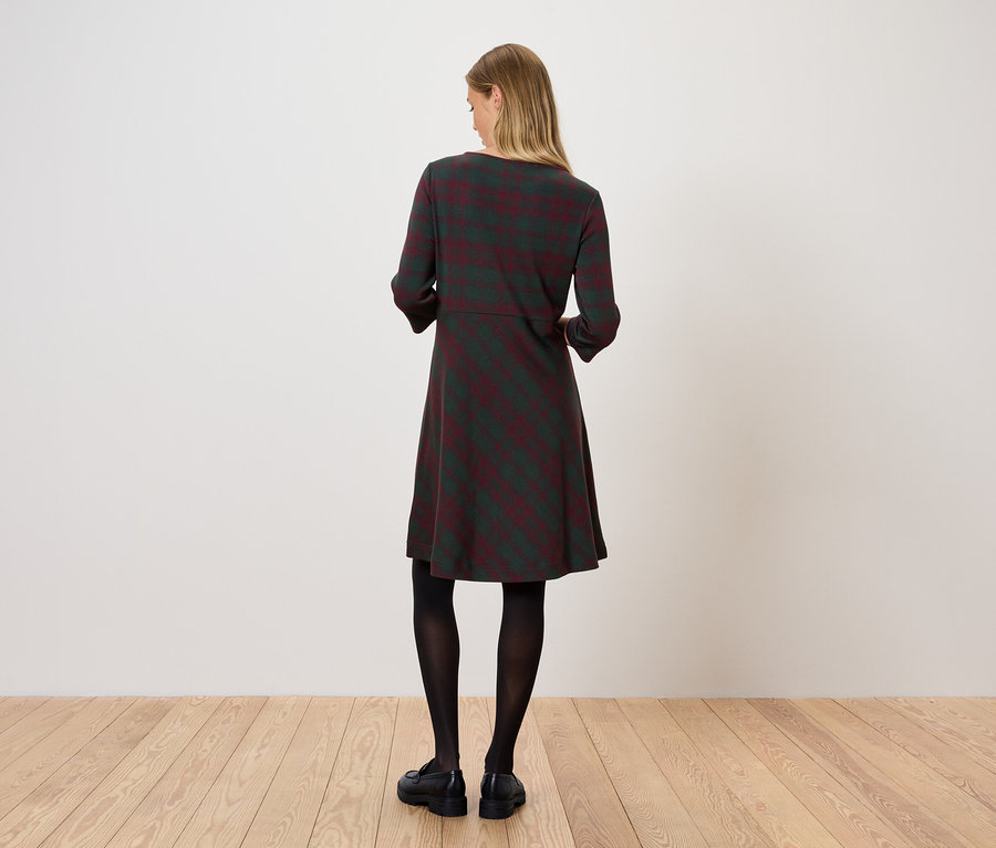 Egy nő háttal áll a kamerának, csíkos ruhát, fekete harisnyát és fekete cipőt visel.