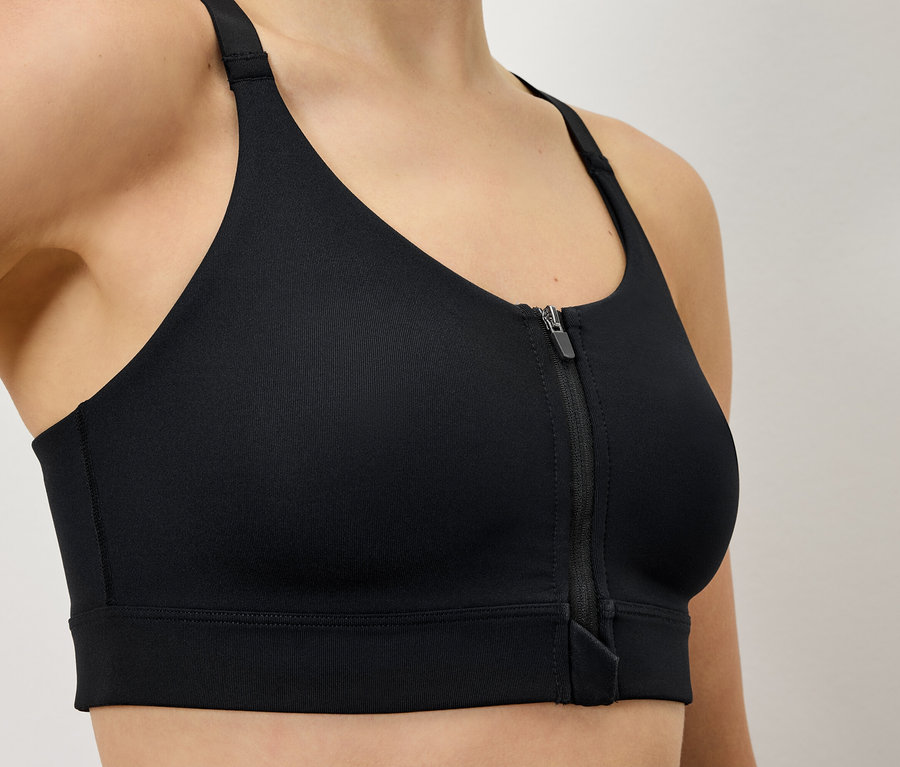 Egy nő fekete sportmelltartót visel, elöl cipzárral.