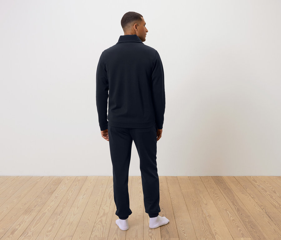 Egy férfi hátulról sötétkék pizsamát és fehér zoknit visel.