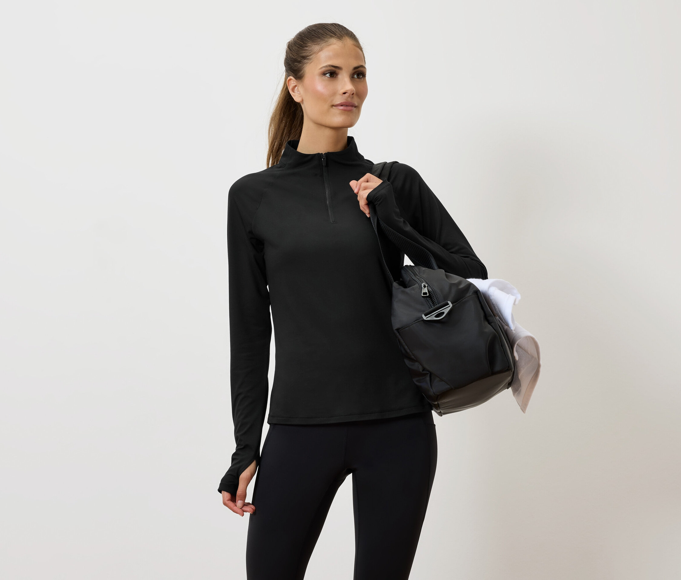 Nő fekete sportruházatban, táskával a vállán.