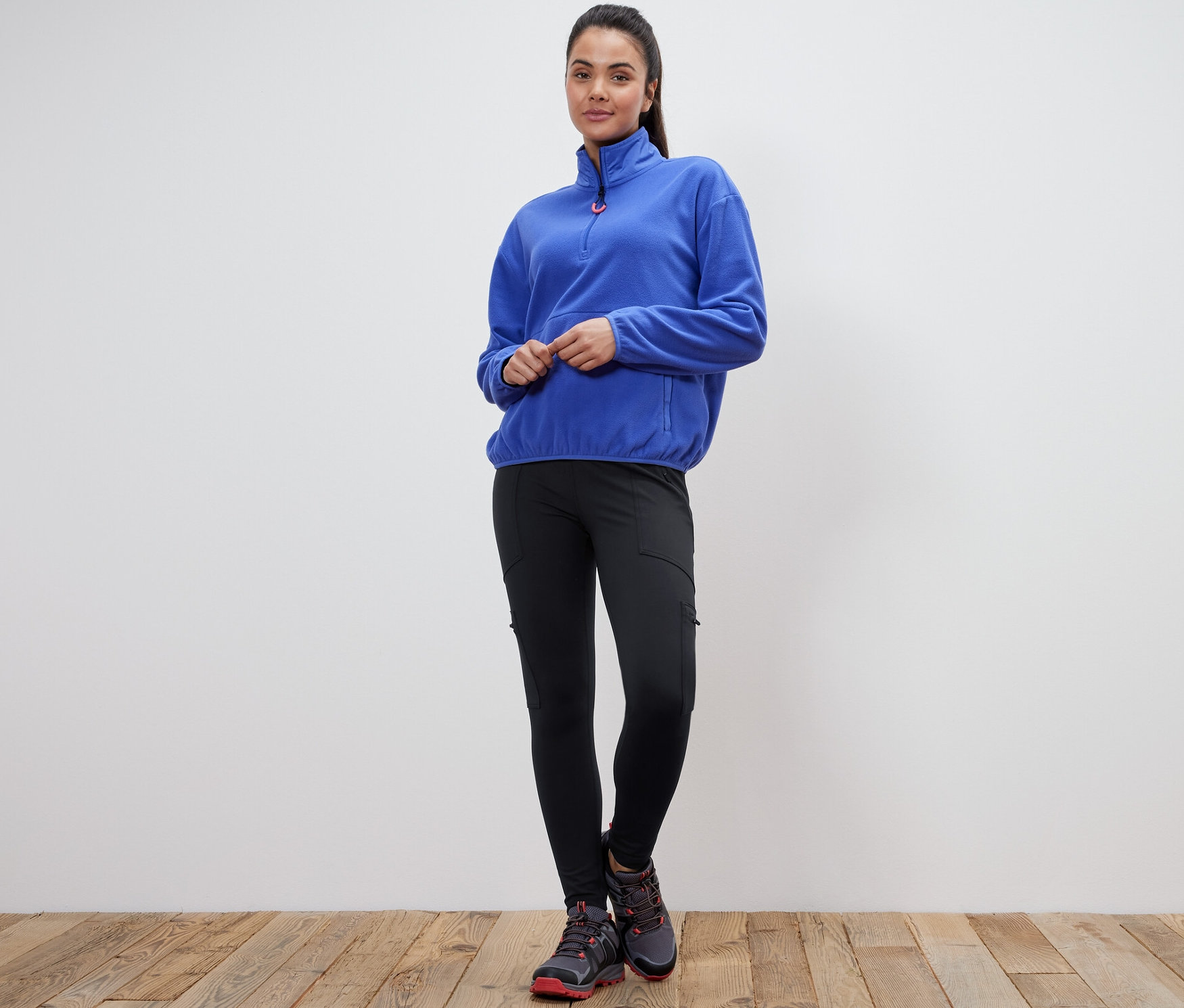 Nő áll, kék polár pulóvert és fekete túranadrágot visel.